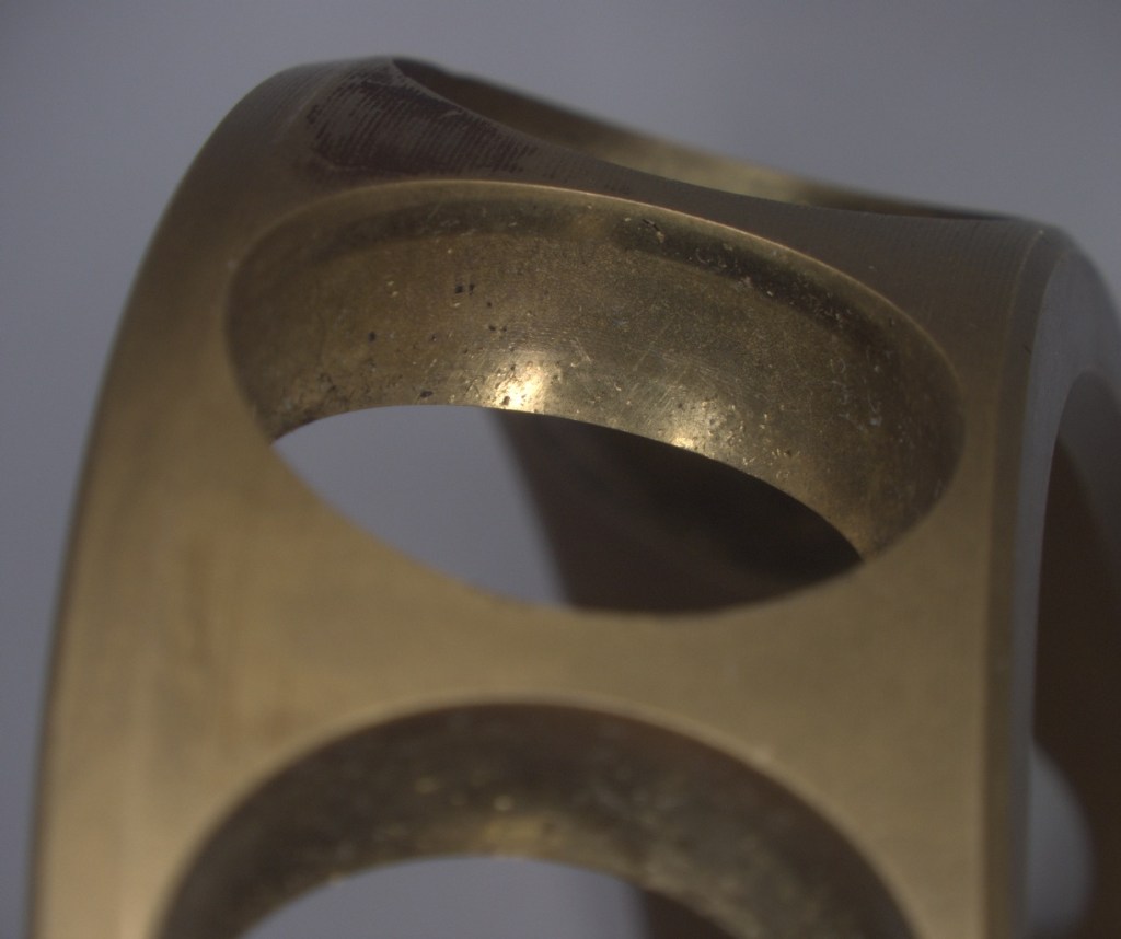 Close-up of a metallic object with a smooth, shiny surface and cut-out shapes, reflecting light.