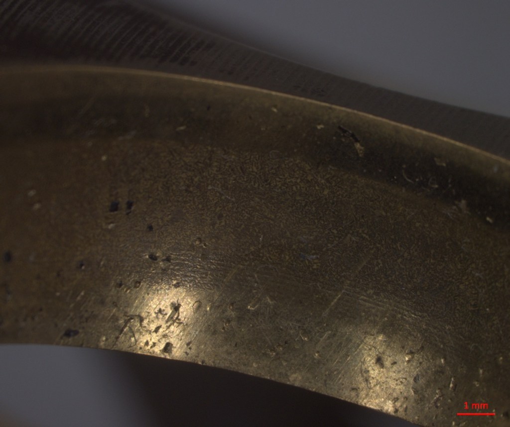 Close-up of a metallic surface with visible scratches and texture details, featuring a scale indicating 1 mm.
