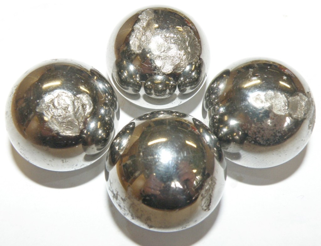Four metallic balls with shiny surfaces, showing some wear and reflections.